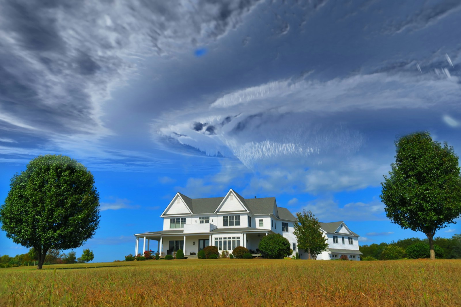 white and gray house between two green tall trees under gray clouds forming swirl during daytime hurricane home